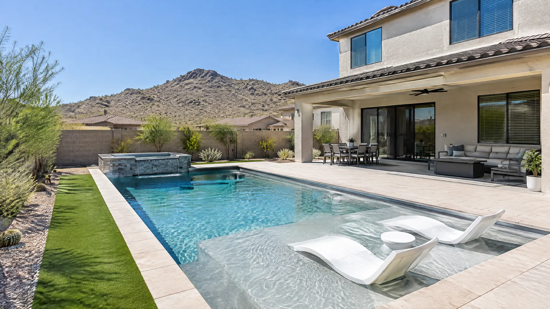 Newer two-story stucco home backyard in Stetson Valley, northwest Phoenix: geometric pool with a baja shelf, light gray finish, artificial turf strip, low desert hills in the distance