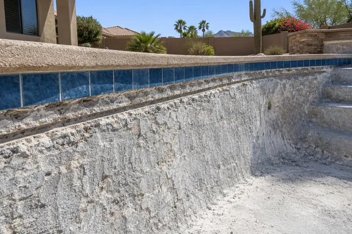 Empty pool wall with old plaster chipped back and the surface roughened, a straight cut groove under the tile line, ready for a new finish, no workers visible