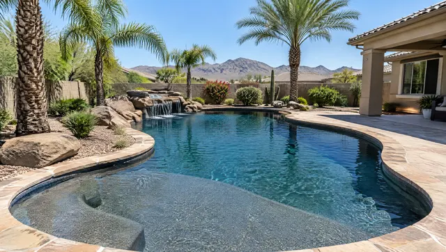 Backyard pool in Phoenix, Arizona with a new dark blue-gray pebble finish giving the water a deep lagoon color, a tanning ledge, flagstone coping, queen palms and gravel desert landscaping