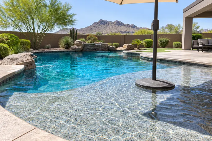 Shallow tanning ledge in a pool with a pebble finish, an umbrella base, clear water
