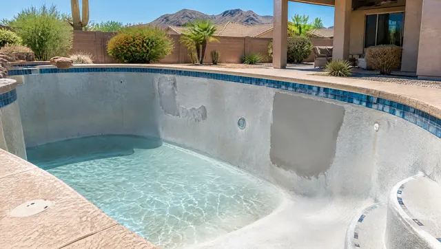 Partly drained residential swimming pool in Phoenix with a repaired section of plaster on the wall, a patched area smoothed and ready for resurfacing, sunlight on the empty pool floor