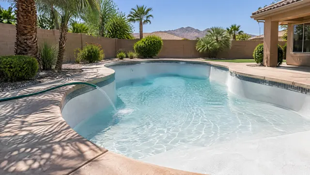 Pool in a Phoenix backyard being refilled with a garden hose after resurfacing: shallow clear water across a fresh white plaster floor, the hose draped over the coping, palm shadows on the deck